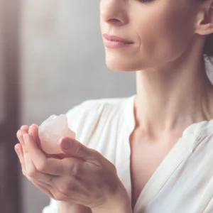 Femme apaisée tenant un cristal brut de quartz rose entre ses mains, symbole de douceur, d’amour et de guérison émotionnelle.