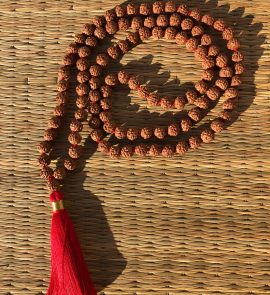 Collier mala 108 perles en graines de rudraksha naturelles, agrémenté d’un pompon rouge symbolisant la vitalité et la force spirituelle. Bijou traditionnel indien utilisé pour la méditation et la prière.