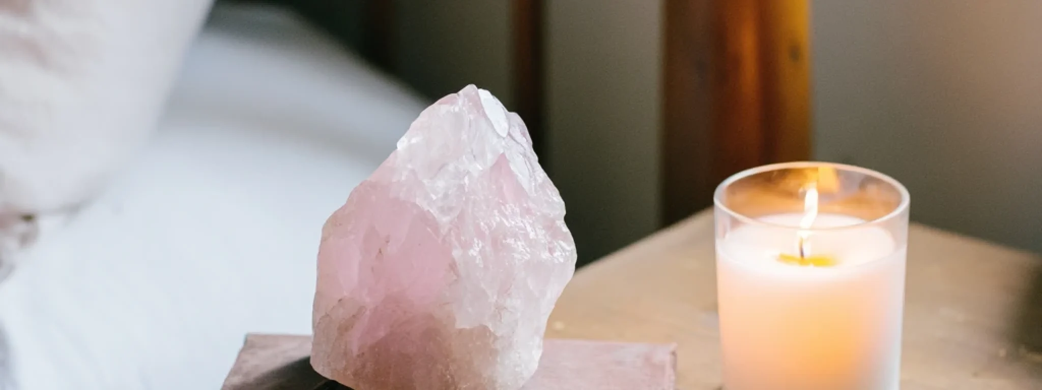 Pierre brute de quartz rose posée sur un livre et accompagnée d’une bougie allumée sur une table de chevet, atmosphère paisible et spirituelle